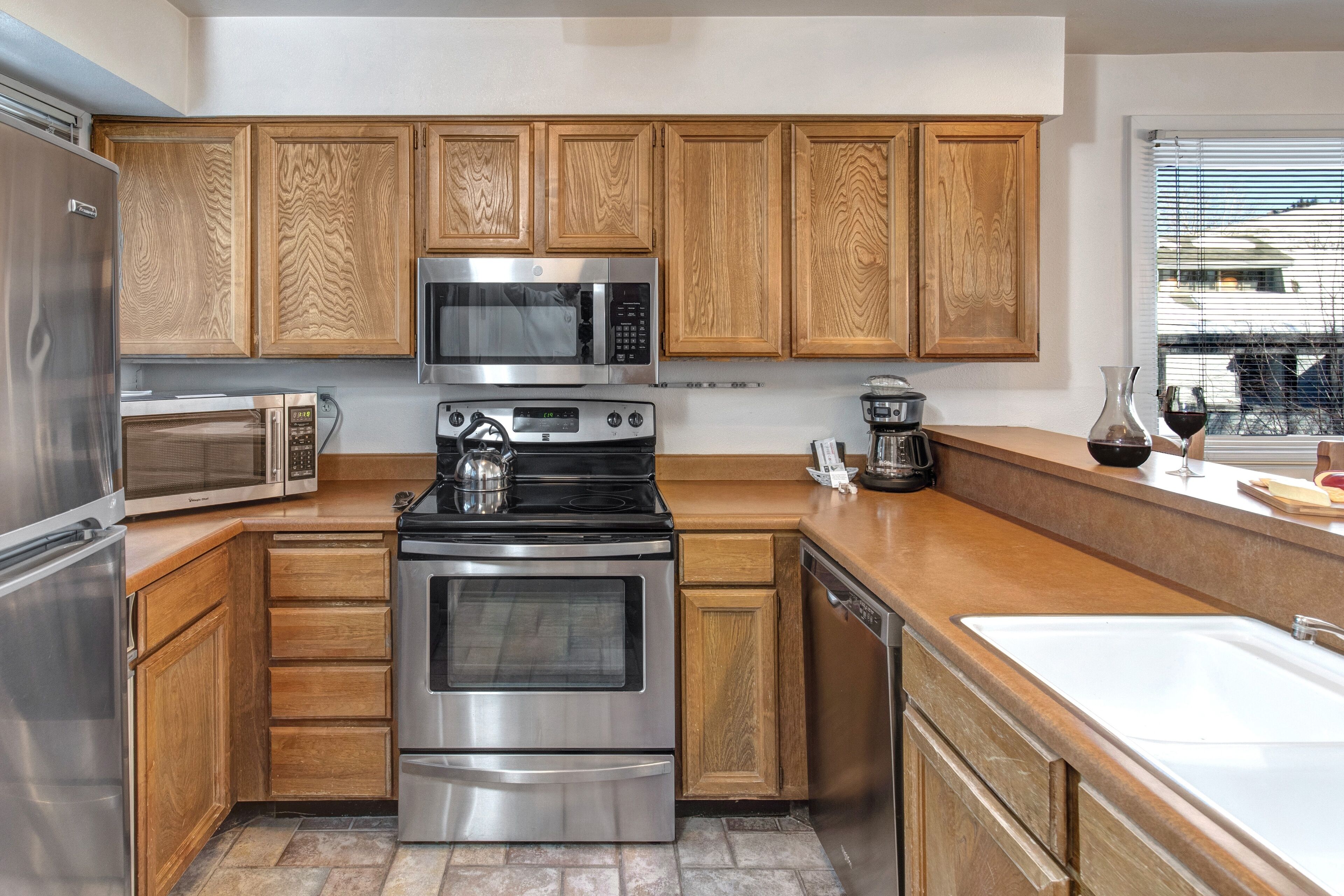 A modern kitchen with wooden cabinets, stainless steel appliances, and a large window.