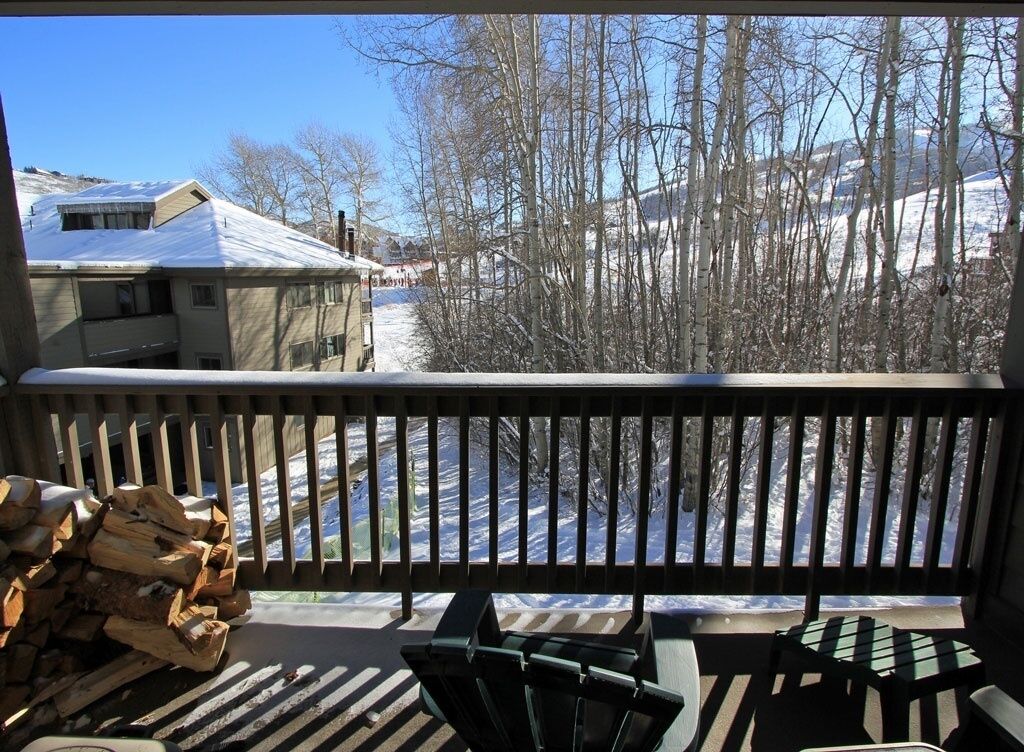 A balcony with a view of a snowy landscape, a stack of firewood, and outdoor furniture.