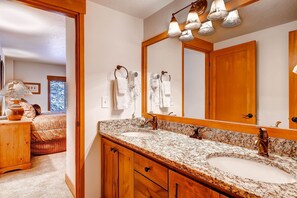 A bathroom with a granite countertop, two sinks, a large mirror, and a ceiling light fixture.