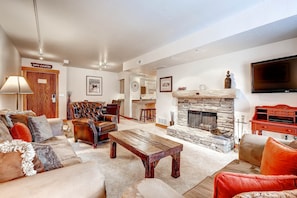 A spacious living room with a fireplace, leather sofas, a wooden coffee table, and a television mounted on the wall.