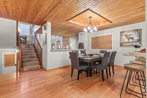 Un comedor con una escalera de madera, una araña y una mesa con sillas.