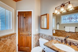 Un baño con puerta de madera, un inodoro, un lavabo con espejo y una ventana con vitrales.