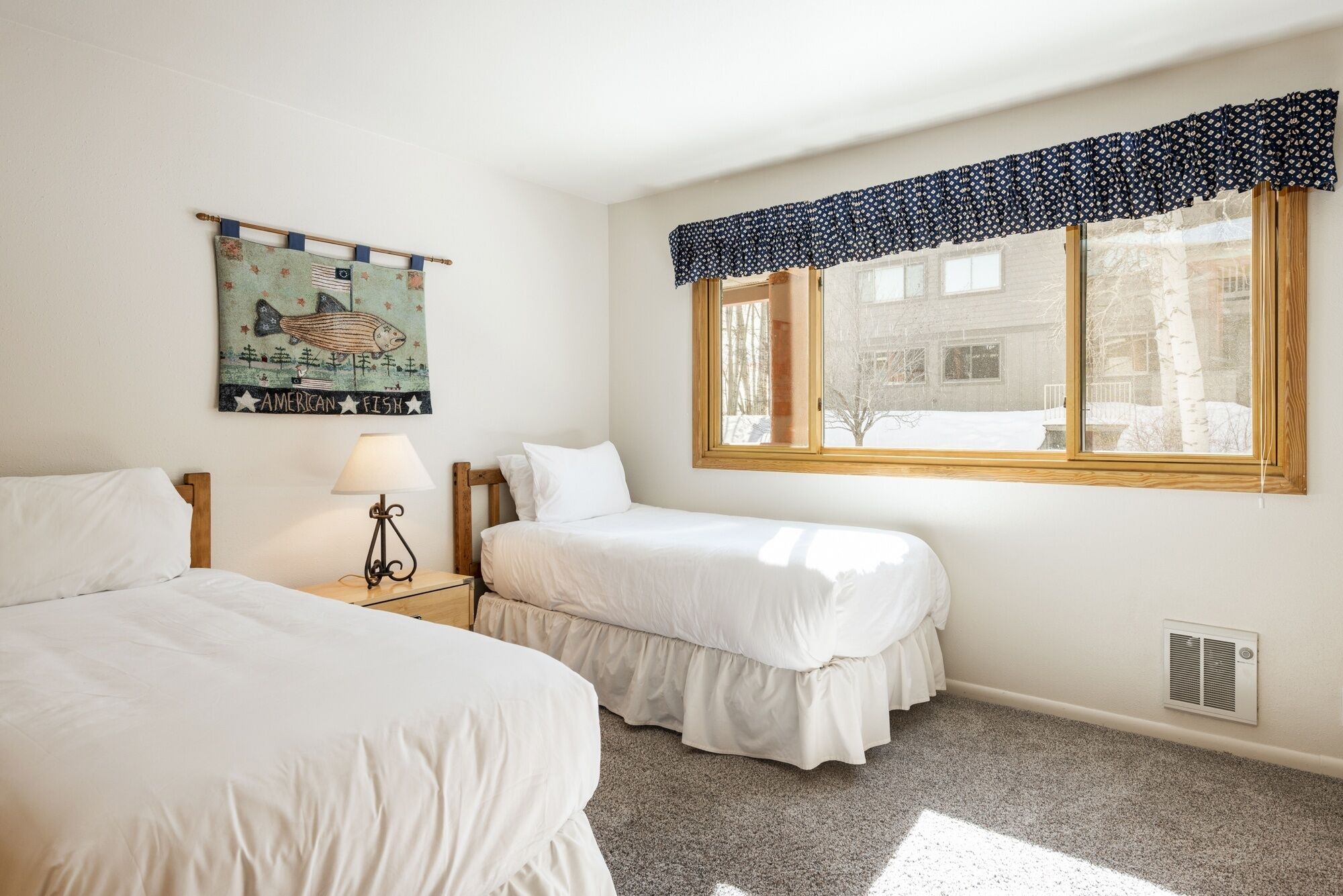 A bedroom with two beds, a window with a view of a snowy landscape, a wall-mounted lamp, and a decorative fish painting.