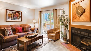 Ein Wohnzimmer mit Sofa, Sesseln, Kamin und einem großen Fenster mit Vorhängen.
