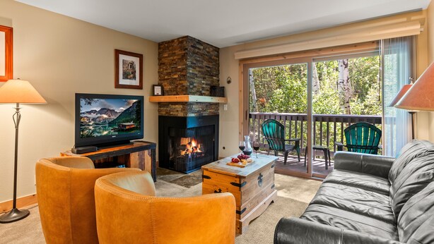 A cozy living room with a fireplace, comfortable seating, and a balcony with outdoor furniture.