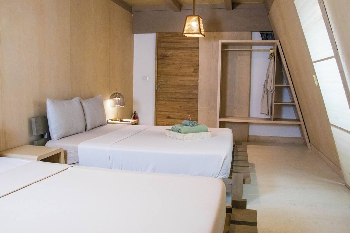 A bedroom with two beds, a wooden wardrobe, a ladder, and a hanging light fixture.
