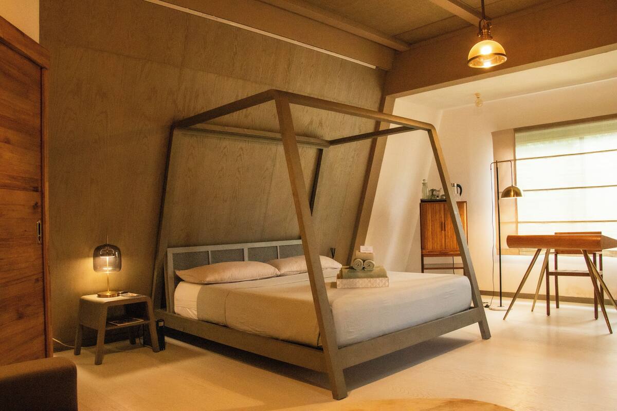 A bedroom with a four-poster bed, a bedside table with a lamp, and a wooden desk with a chair.