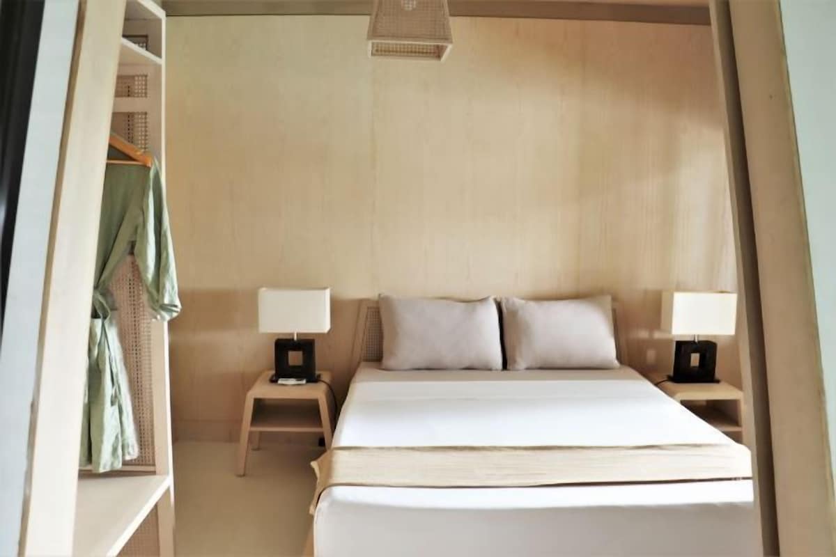 A bedroom with a large bed, two bedside tables with lamps, a hanging light fixture, and a wardrobe.