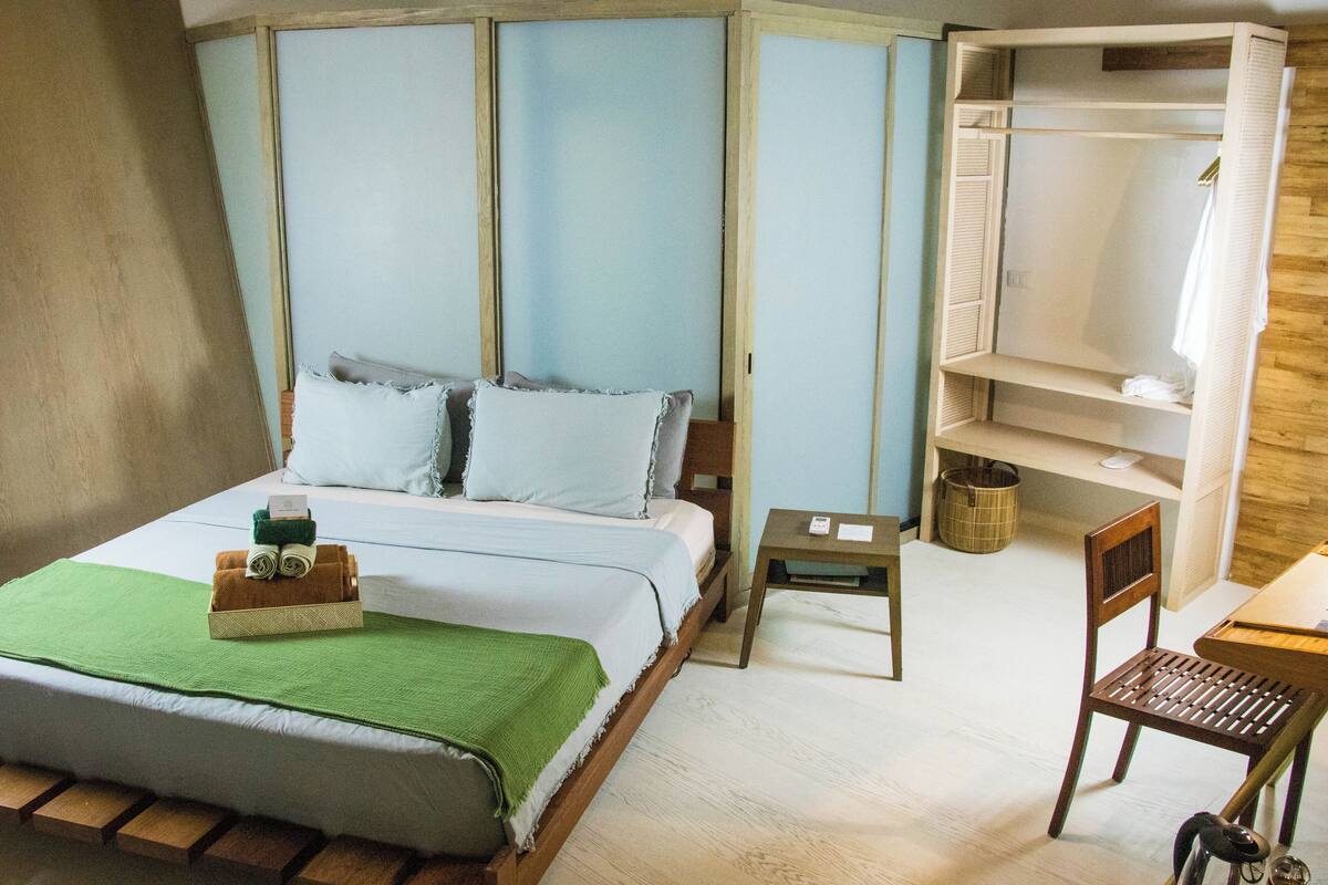 A bedroom with a bed, a chair, a small table, and a wardrobe.