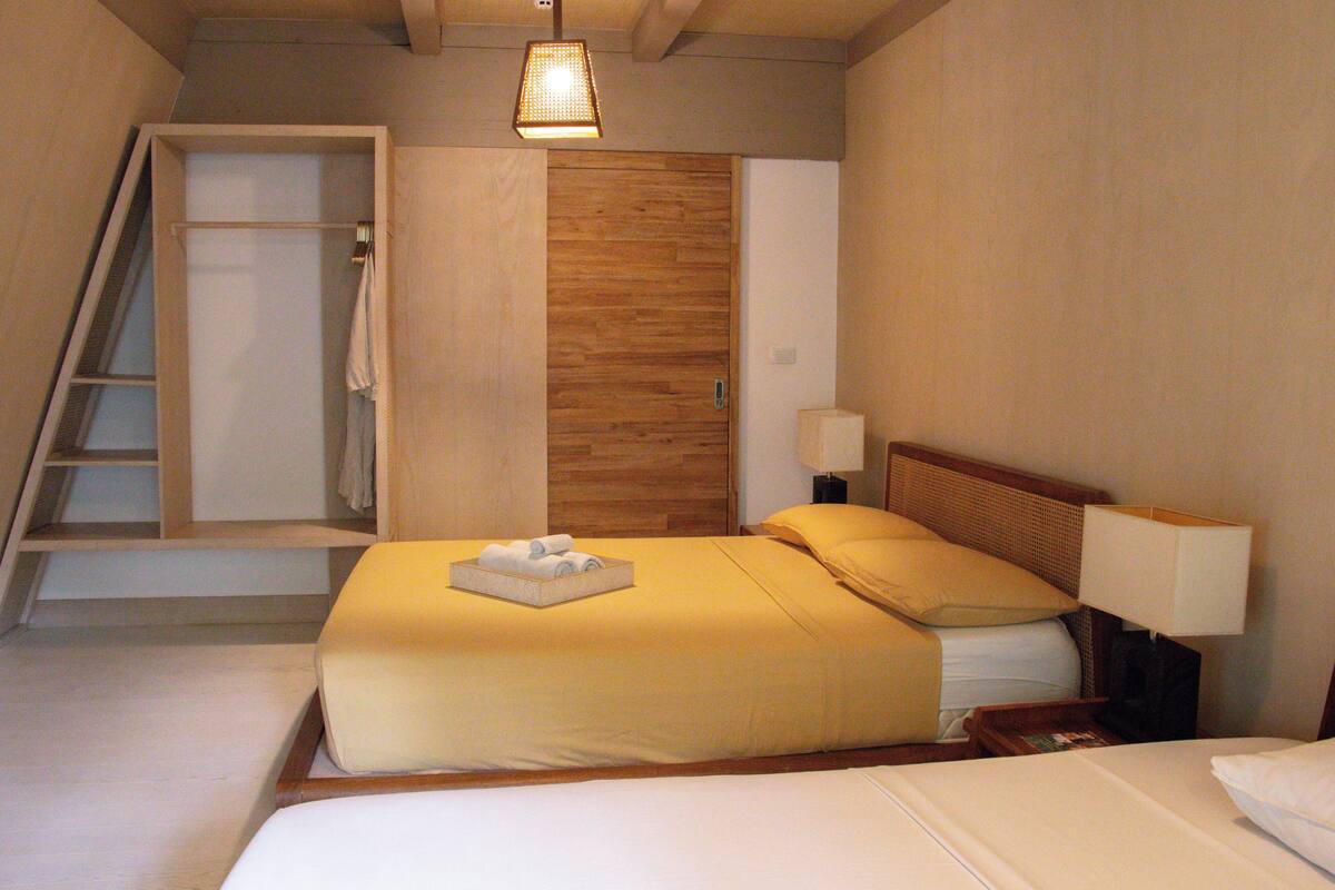 A hotel room with a bed, a nightstand, a lamp, a wooden wardrobe, and a bathroom with a shower and a towel rack.