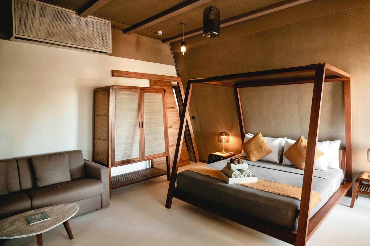 A bedroom with a four-poster bed, a sofa, a small table, and a wardrobe.