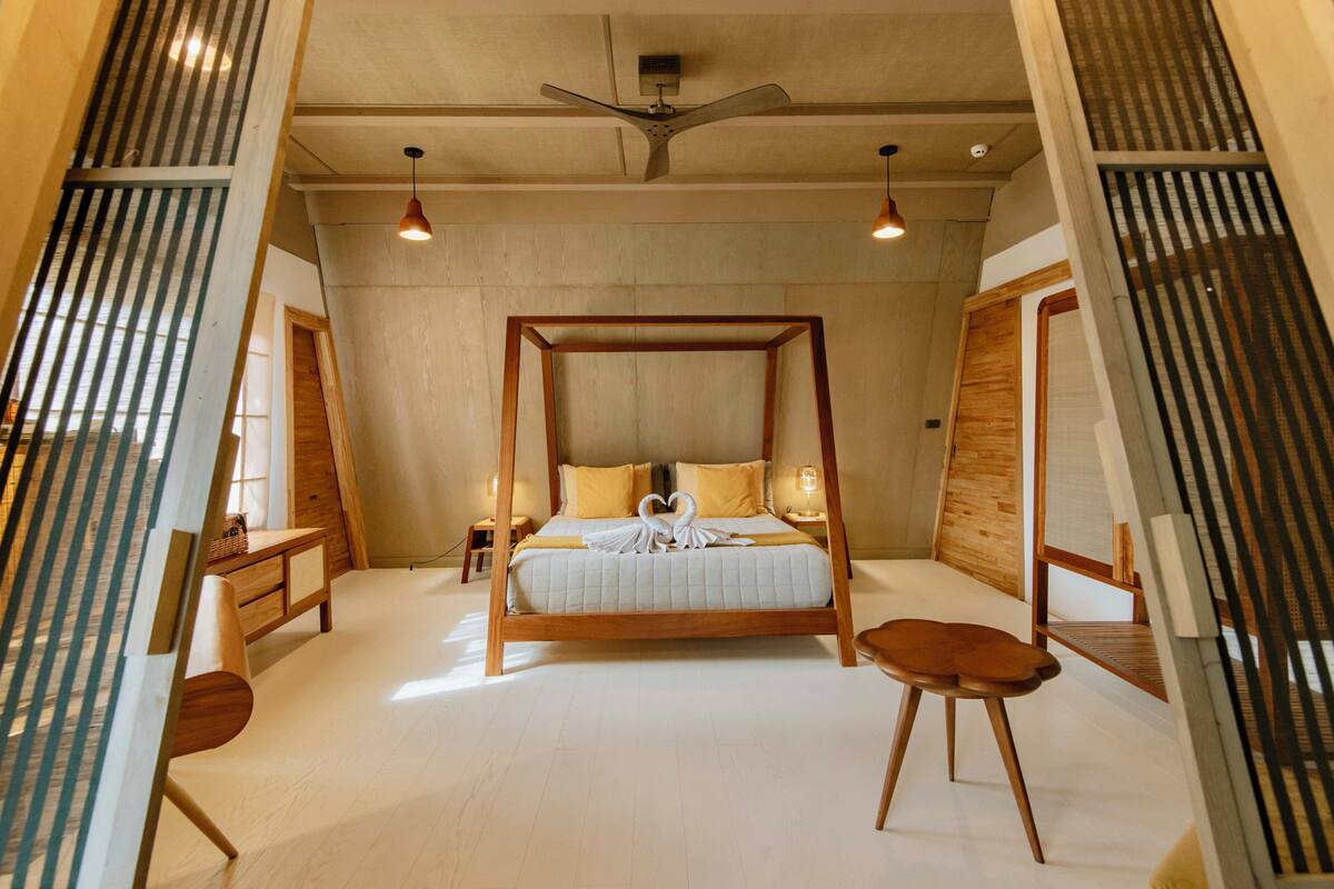 A spacious bedroom with a four-poster bed, wooden furniture, and a ceiling fan.