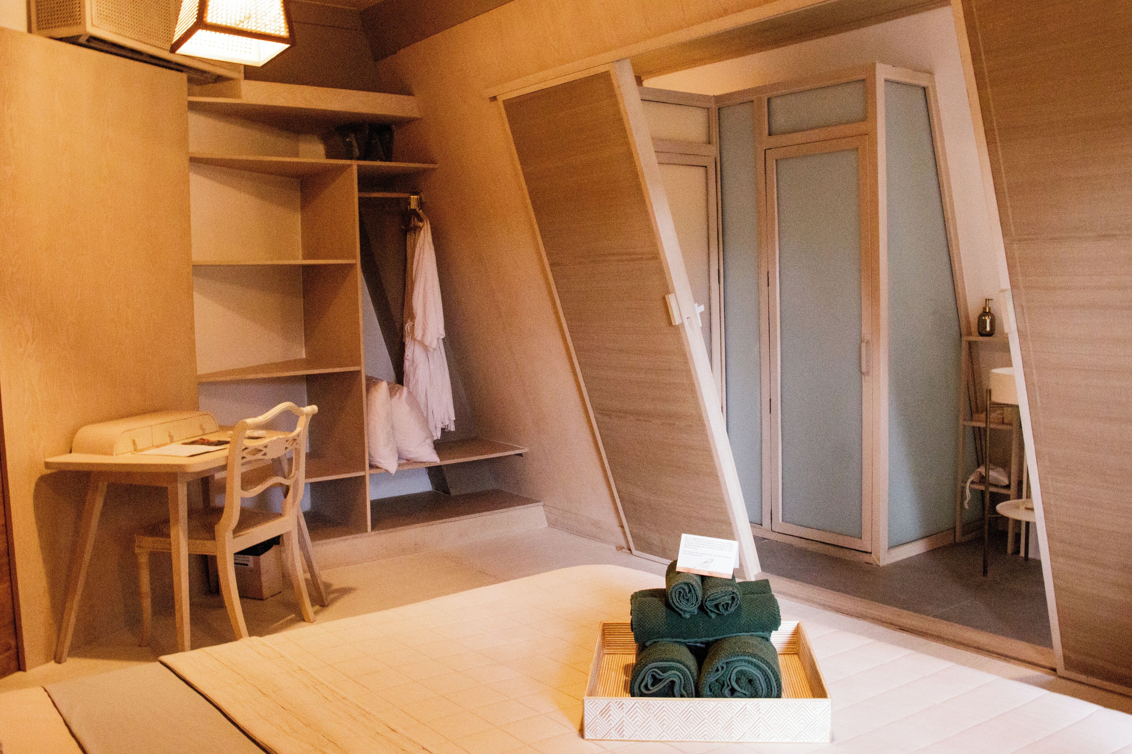 Ein Schlafzimmer mit einem Bett, einem Schreibtisch und einem Stuhl. Es gibt einen Holzschrank und einen kleinen Tisch mit einer Lampe.