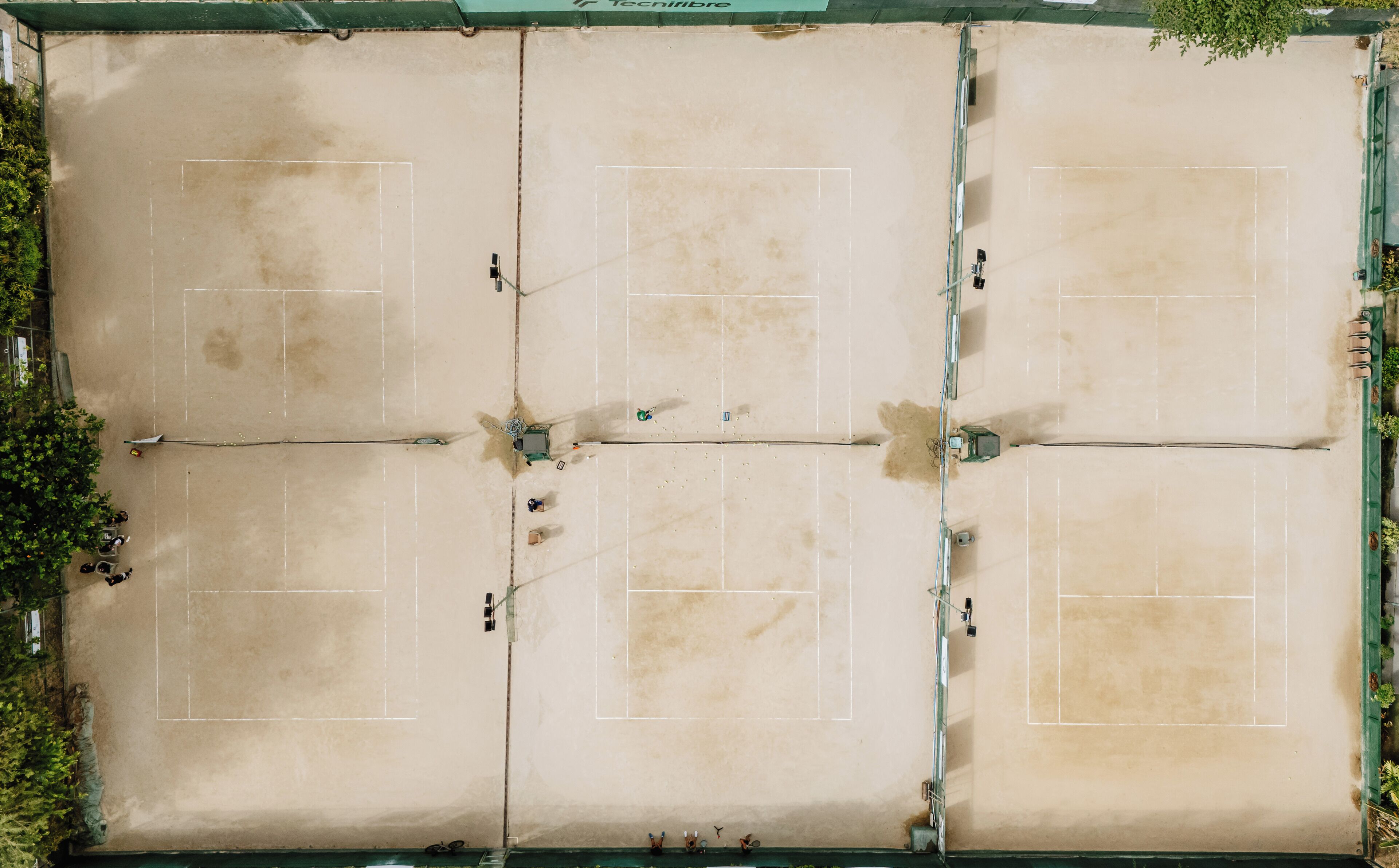 An aerial view of a tennis court with four sections, surrounded by greenery.