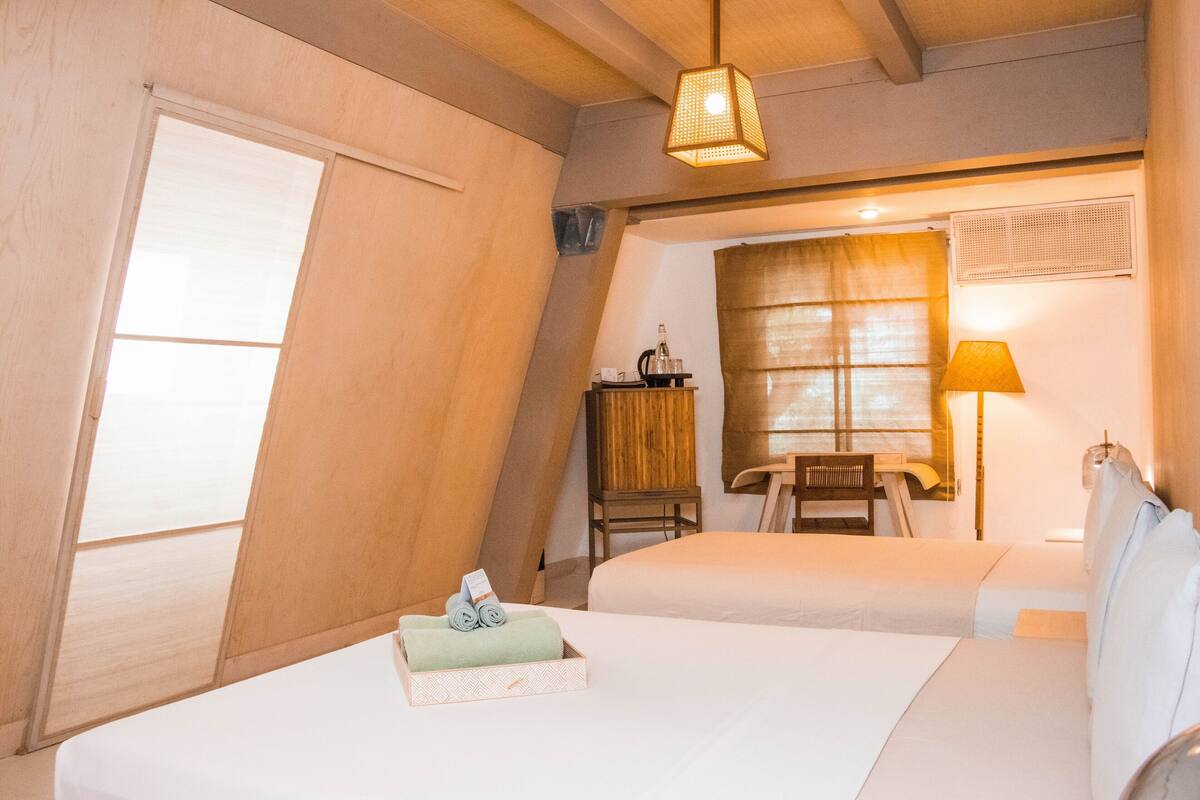 A hotel room with two beds, a desk, a chair, a lamp, and a window with curtains.