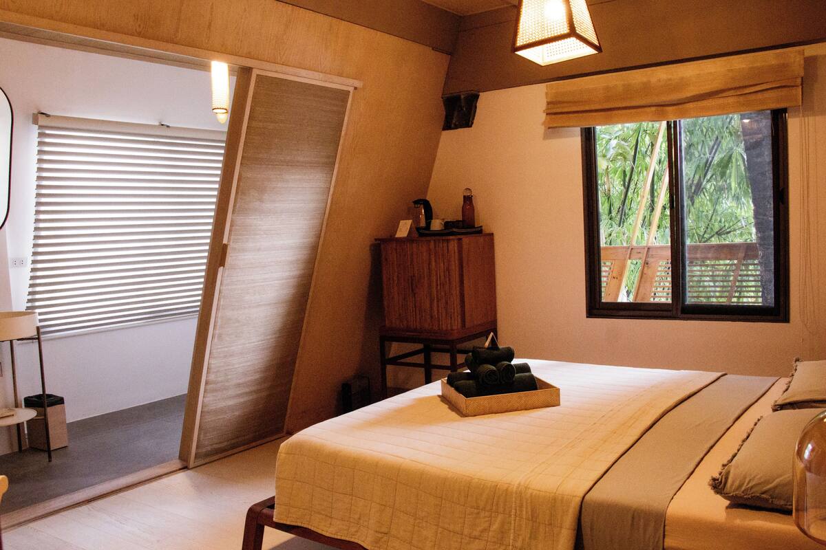 A bedroom with a bed, a wooden nightstand, a window with a view of greenery, and a sliding door.