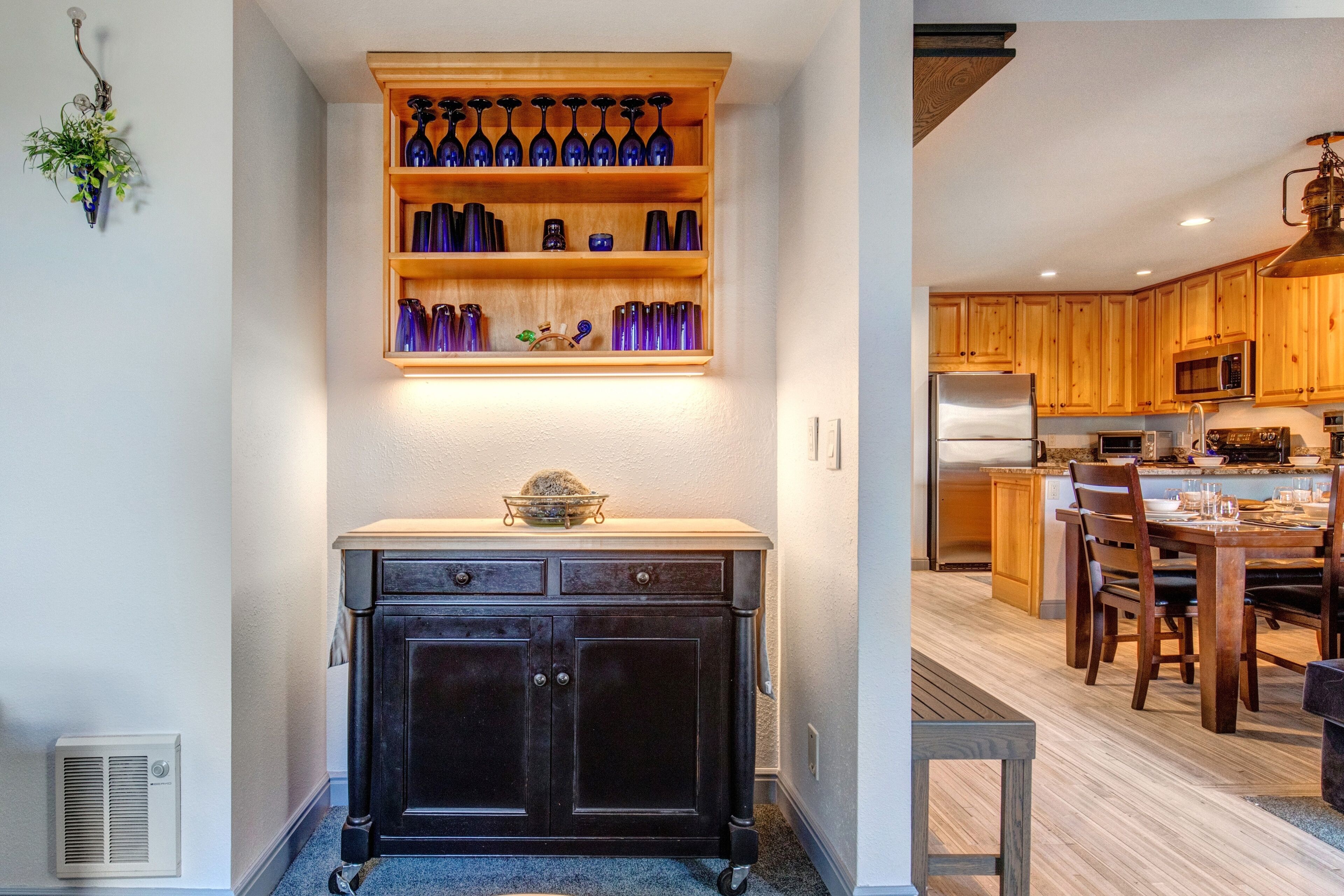 A kitchen with wooden cabinets, a built-in shelf with blue glassware, and a dining area with a table and chairs.