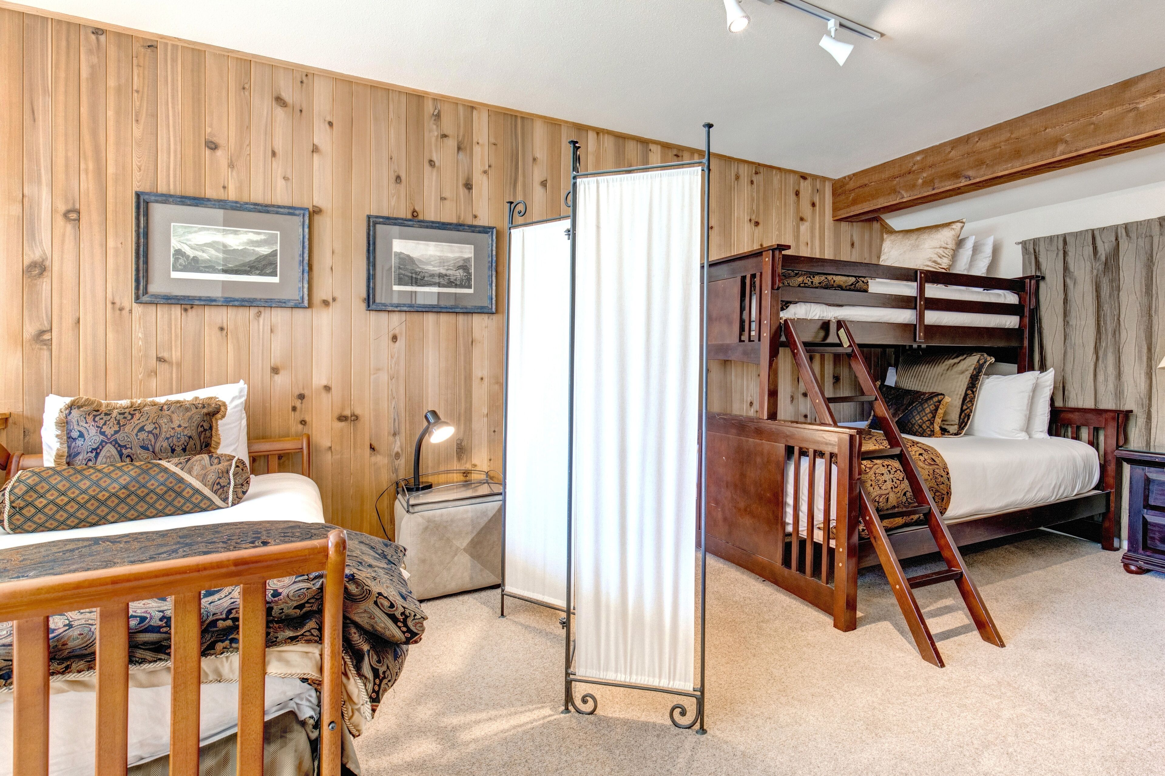 Quarto com beliche, escrivaninha com luminária e cama com roupa de cama estampada.