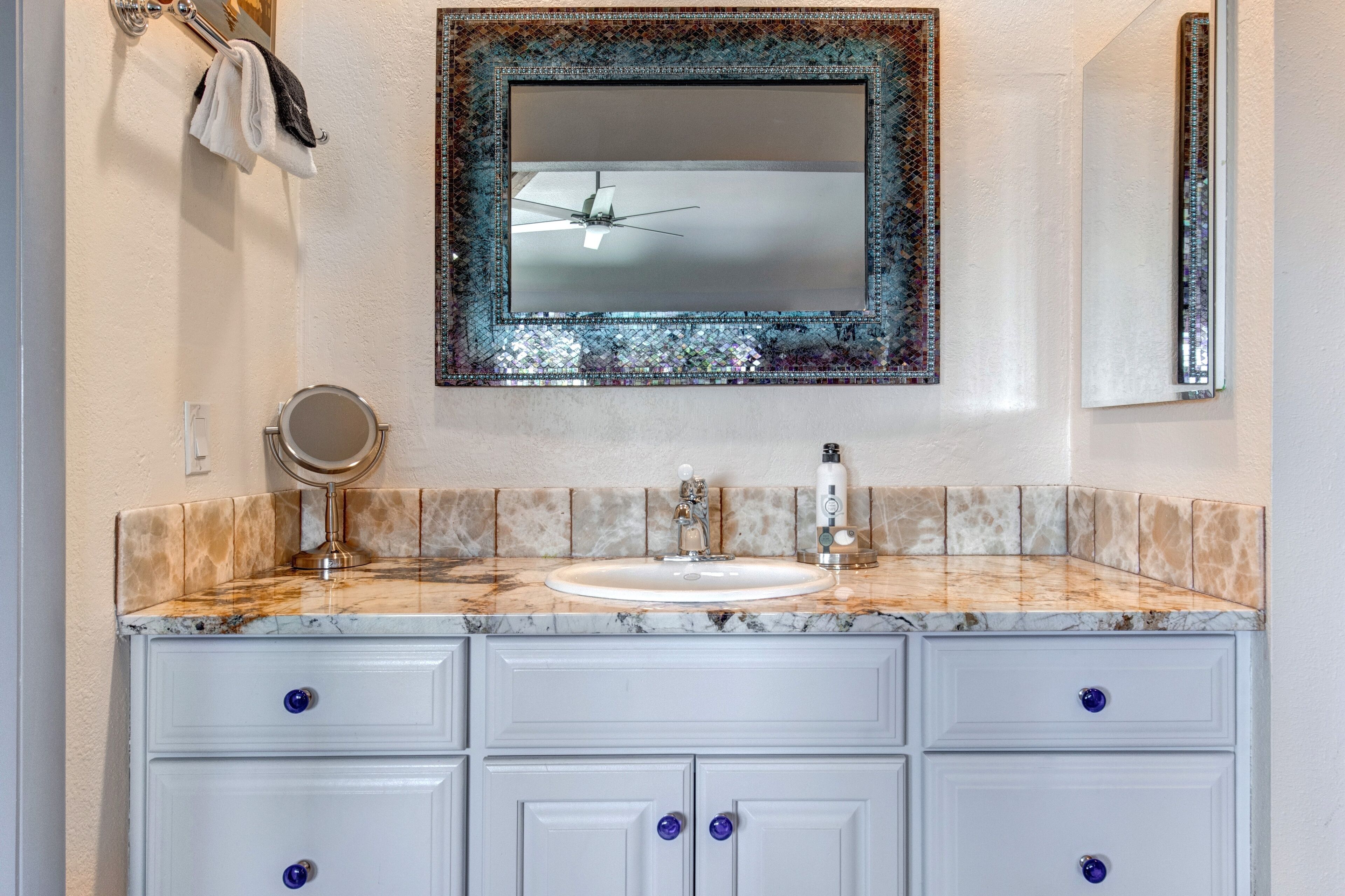 A bathroom with a marble sink, a mirror, and a ceiling fan.