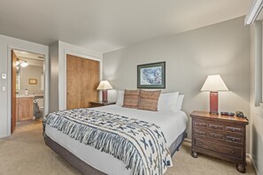 A bedroom with a large bed, two bedside tables with lamps, a wooden wardrobe, and a framed picture on the wall. - Snow Flower 140 2 Bedroom Condo by RedAwning (Park City)