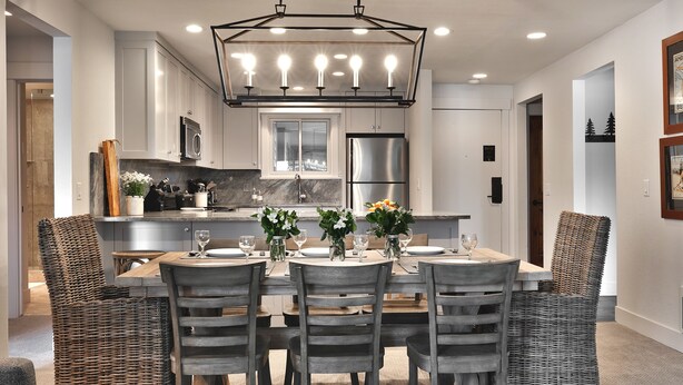 A modern kitchen with white cabinets, a stainless steel refrigerator, and a dining area with wicker chairs and a wooden table.