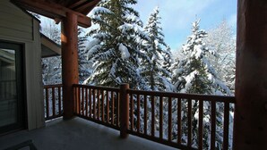 A wooden balcony with a railing overlooking snow-covered trees.