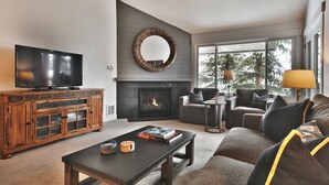 A modern living room with a flat-screen TV, a fireplace, a large mirror, and a cozy seating area.