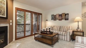 A living room with a fireplace, a sofa, a coffee table, and artwork on the wall. - Snow Flower 111 2 Bedroom Condo by RedAwning (Park City)