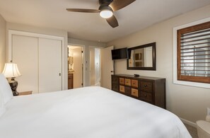 A hotel room with a bed, a dresser, a ceiling fan, a TV, a mirror, and a window with blinds. - Snow Flower 111 2 Bedroom Condo by RedAwning (Park City)