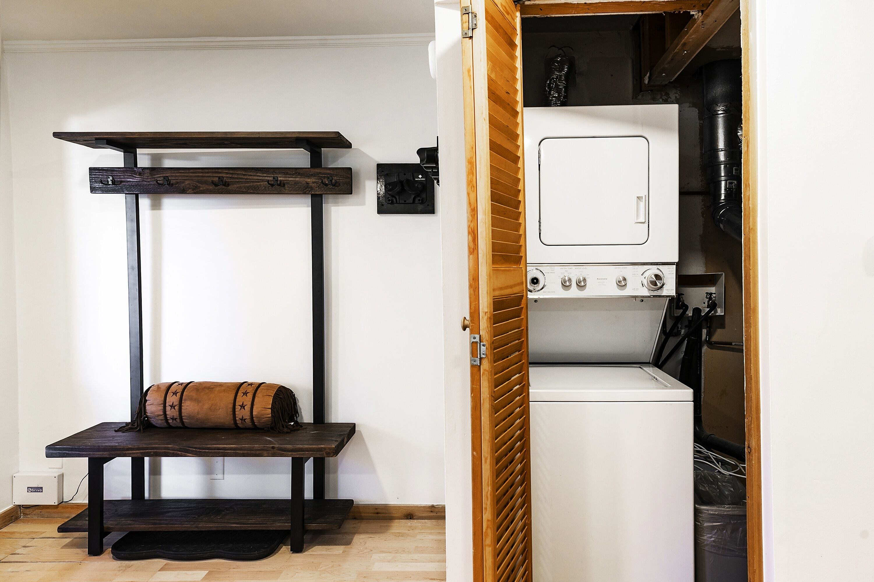 A laundry room with a white washing machine, a wooden bench, and a towel.