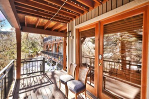 A wooden deck with a railing, a chair, and a large sliding glass door with a view of trees and a building.