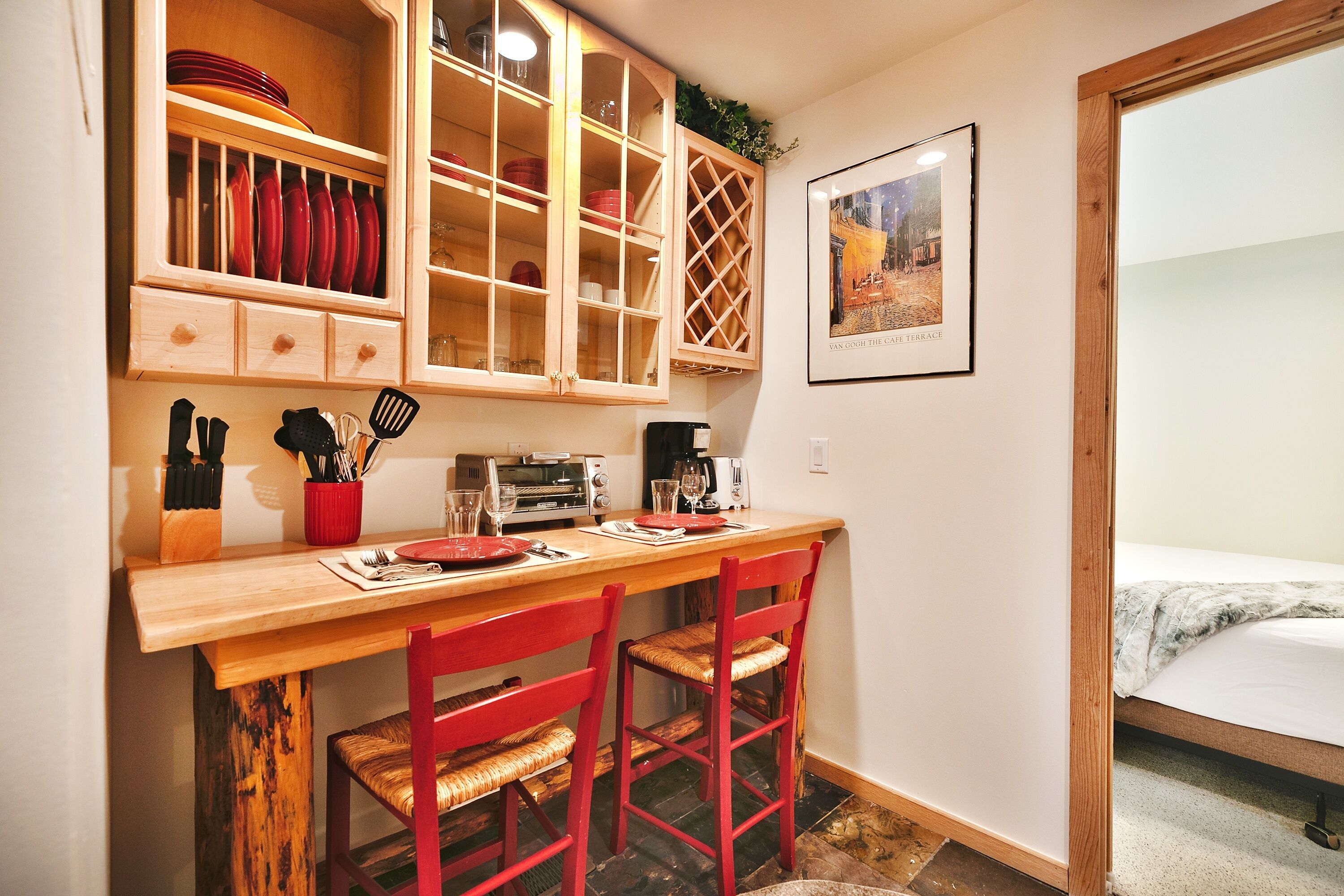 A compact kitchen with wooden cabinets, a dining table, and red chairs.