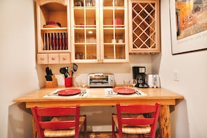 Compact kitchen area with a table for two, featuring a toaster oven, coffee maker, and wine rack.