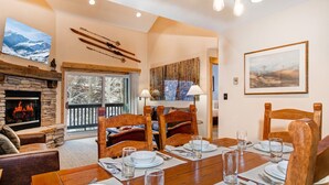 A dining area with a stone fireplace, wooden chairs, and a table set for four.