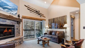 A cozy living room with a stone fireplace, leather furniture, and a large window overlooking a snowy landscape.
