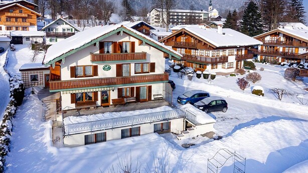 Ein mehrstöckiges Chalet mit Balkon, umgeben von schneebedeckten Bäumen und Bergen.