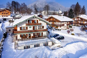 A multi-story chalet with a balcony, surrounded by snow-covered trees and mountains. - Ferienhaus Ostara Balk/terr., 6 Schlafz.m. Du/wc, 1 Wohnz., Aufenthaltsraum, Max. 12 Pers (Ruhpolding)