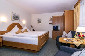 A hotel room with a double bed, a desk with a lamp, a television, and a small table with flowers. - Ferienhaus Ostara Balk/terr., 6 Schlafz.m. Du/wc, 1 Wohnz., Aufenthaltsraum, Max. 12 Pers (Ruhpolding)