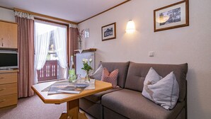 Ein gemütliches Wohnzimmer mit einem braunen Sofa, einem Holztisch mit Zeitschriften, einem Fernseher und einem Fenster mit Vorhängen.