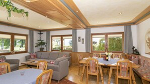 Ein Essbereich mit Holztischen und -stühlen, einer Couch und einem großen Fenster mit Blick auf Grünflächen.
