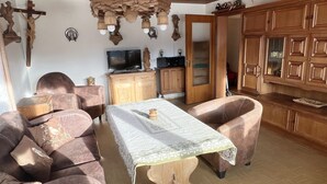 A living room with a wooden dining table, leather sofas, a television, wooden cabinets, and a chandelier.