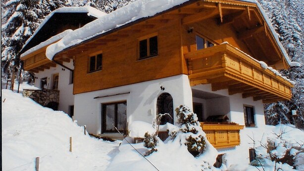 A wooden chalet with a balcony, surrounded by snow-covered trees.
