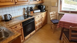 A kitchen with wooden cabinets, a stove, a sink, and a window with a view of trees.