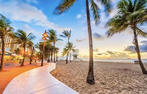 A beach with palm trees, a lifeguard tower, and a walkway.