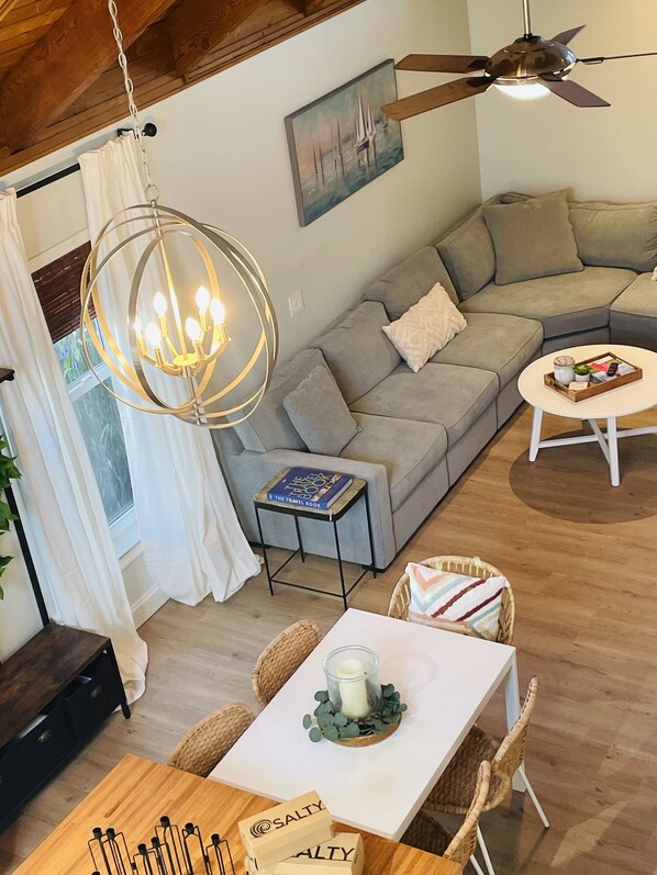 A cozy living room with a grey sofa, a round coffee table, a chandelier, and a painting on the wall.