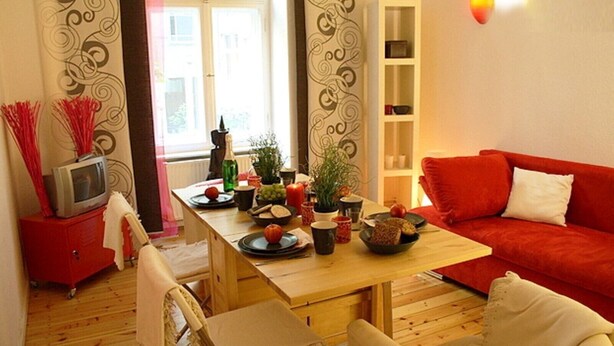 Un salon chaleureux avec une table à manger en bois, un canapé rouge et un téléviseur posé sur un meuble rouge.