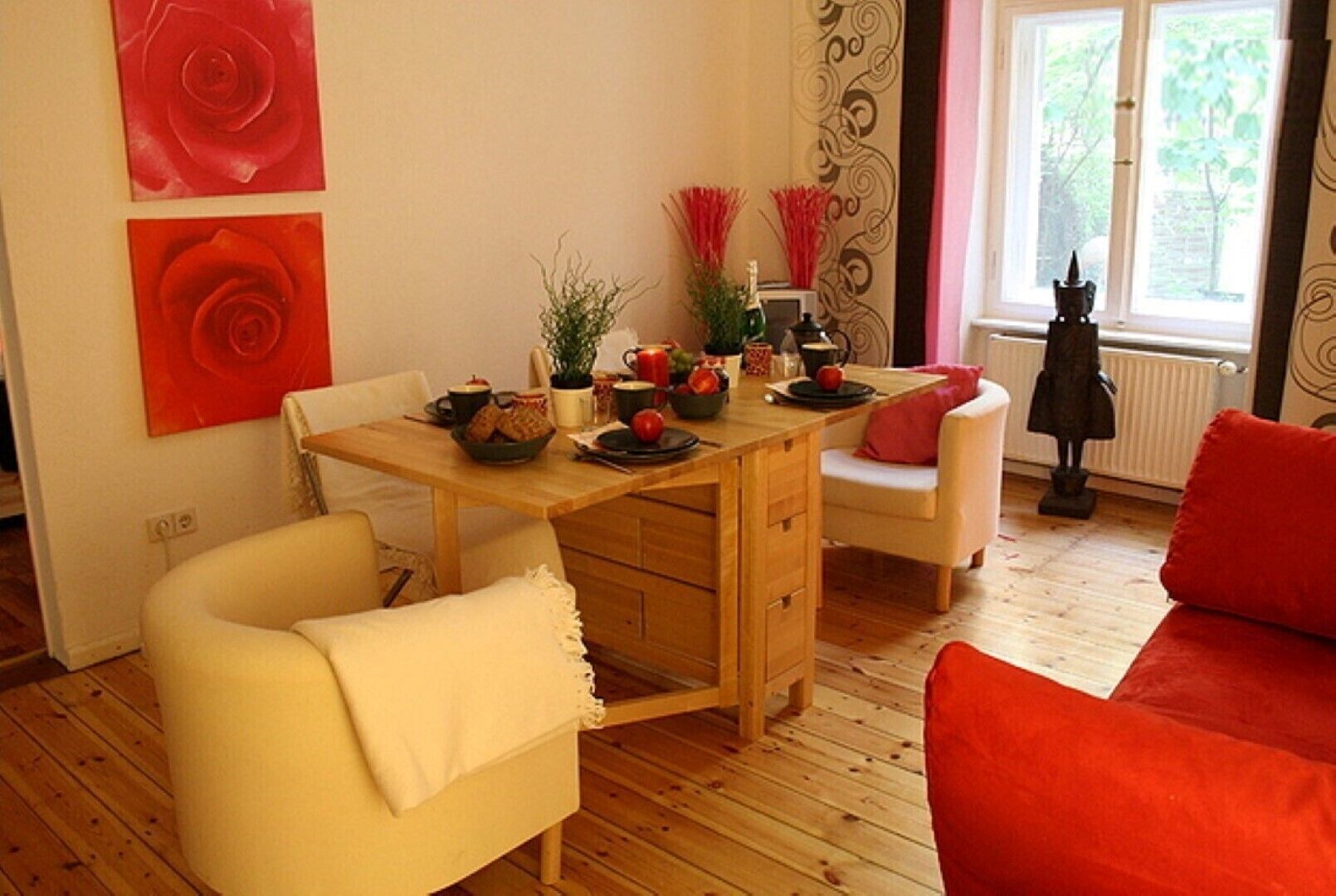 Una sala acogedora con una mesa de comedor de madera, sillones color crema y un sofá rojo.