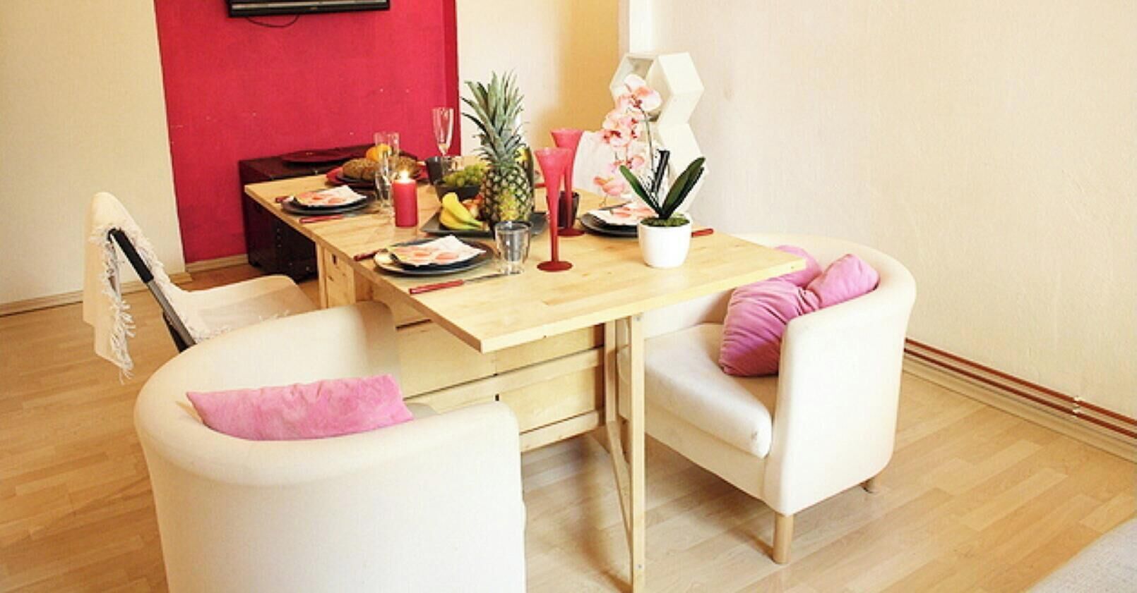 Un comedor con una mesa de madera preparada para dos personas, una planta pequeña en maceta y un frutero.