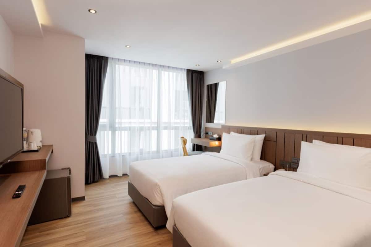 A hotel room with two beds, a TV, a desk, and a window with curtains.