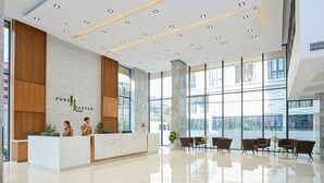 Un moderno área de recepción de hotel con un mostrador de m ármol, detalles de madera y amplias ventanas con vistas a la ciudad.